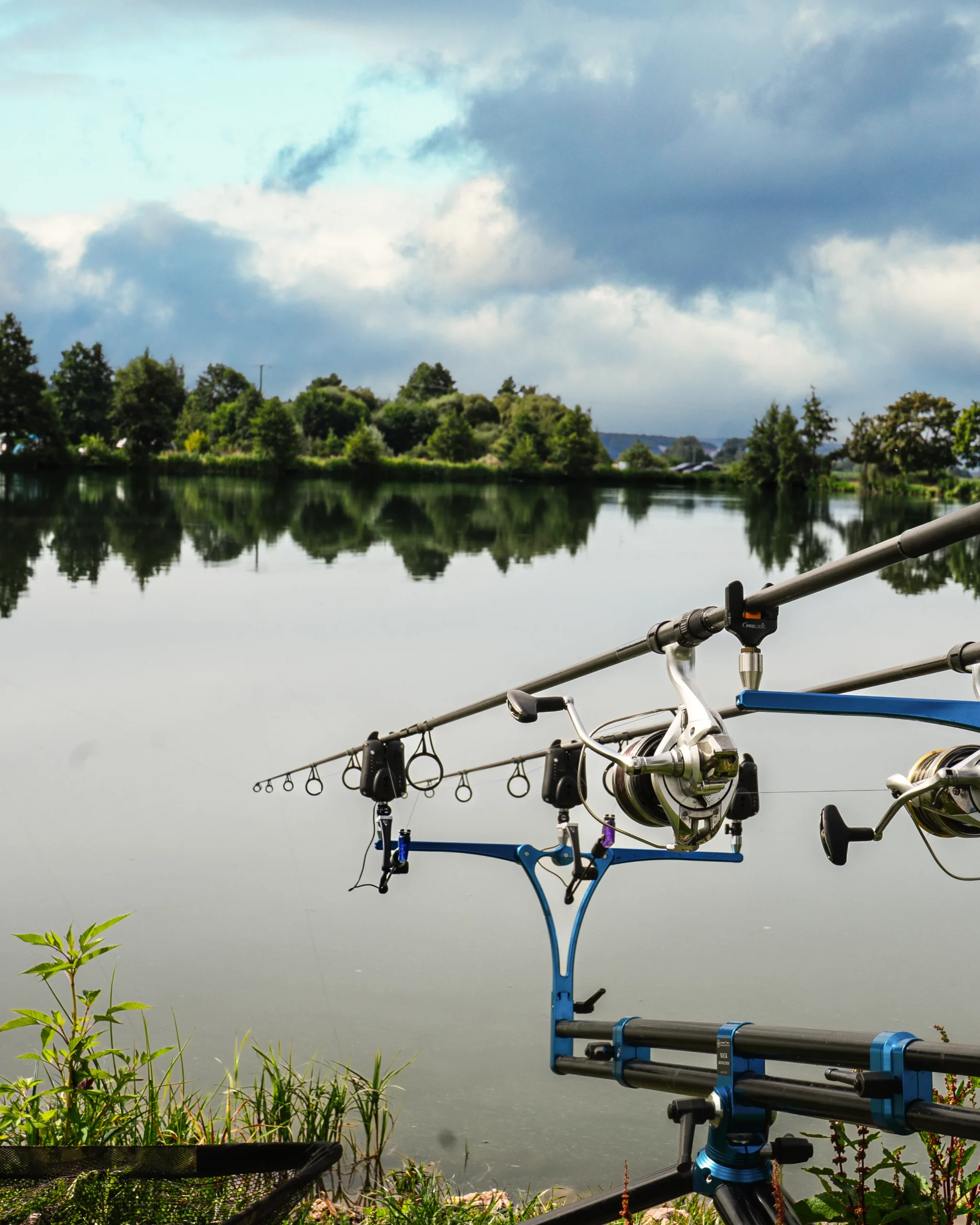 Mehrere Angelruten auf einem Rod-Pod am Ufer eines ruhigen Sees bei Spiegelglattem Wasser