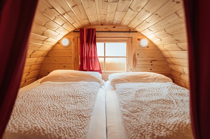 Gemütlicher Innenraum eines Campingfasses mit weichen Betten und heller Holzoptik von Reich am Schnackensee