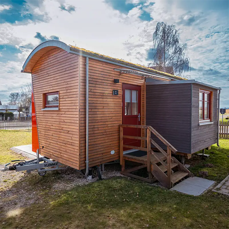 Rustikaler Schäferwagen aus Holz mit roter Tür auf dem Campingplatz am Schnackensee.